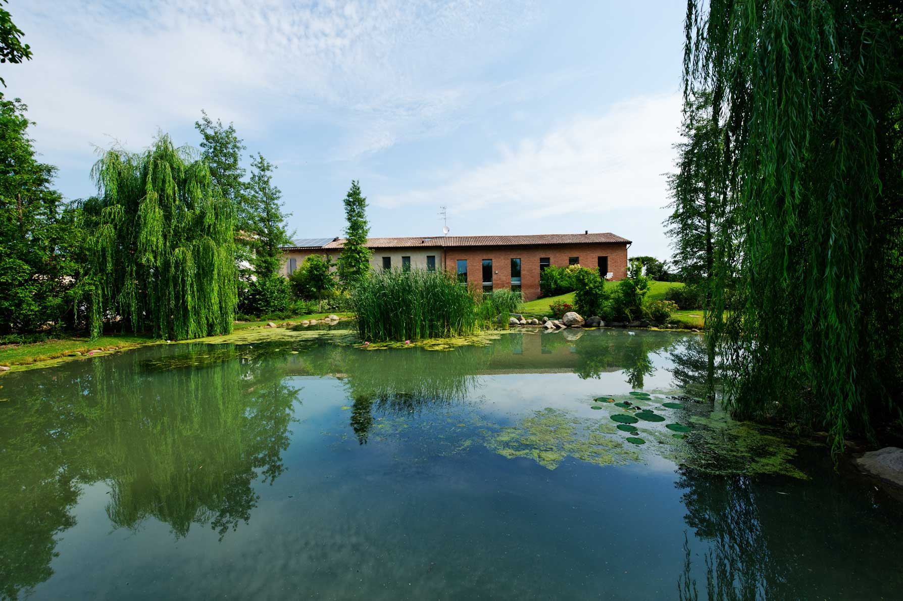 Vista esterna della cascina riqualificata con laghetto e giardino
