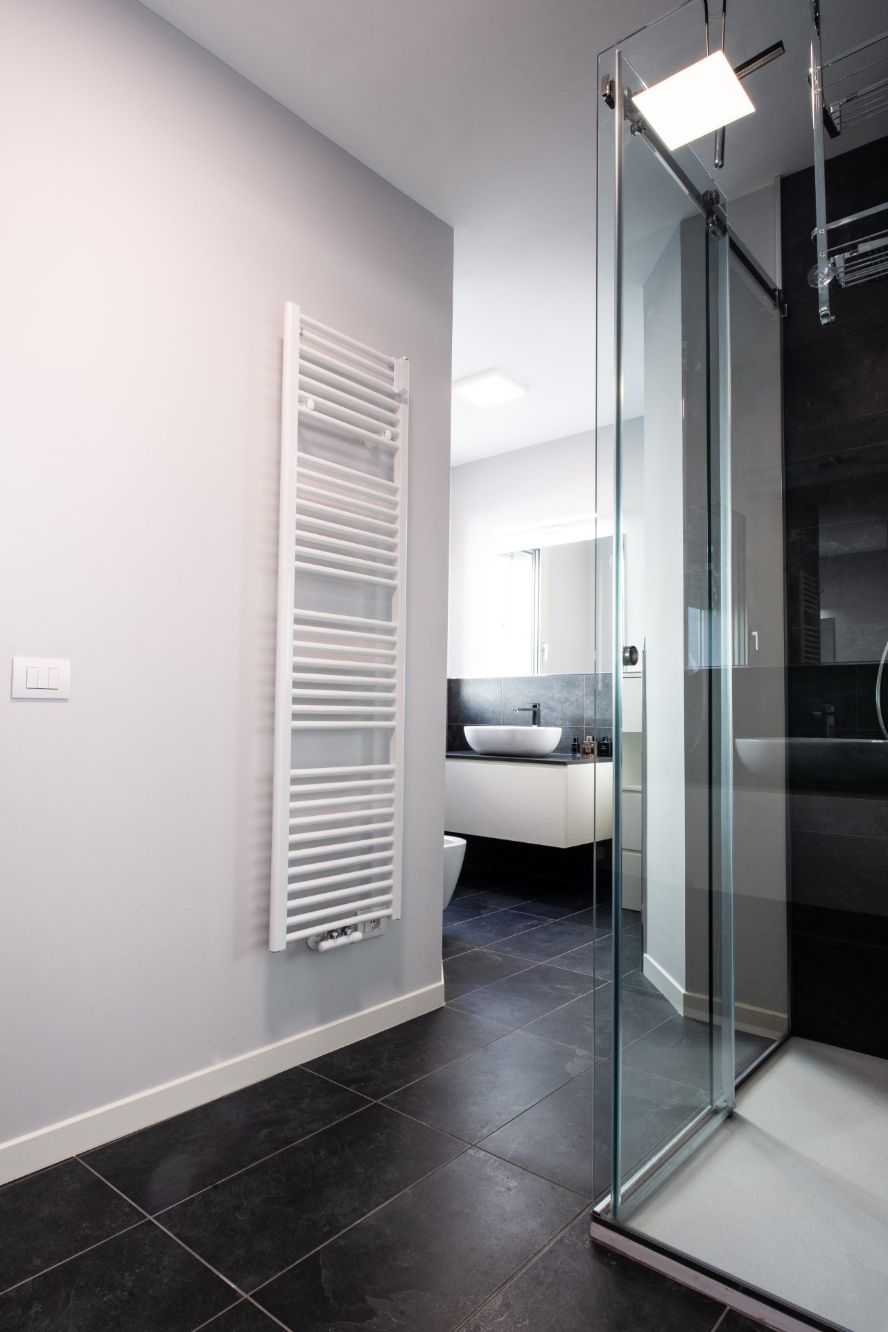 Bagno moderno con rivestimenti scuri, doccia in vetro e termoarredo bianco
